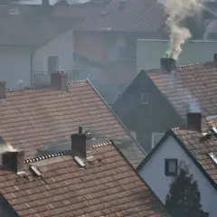 Dym wydobywający się z kominów domów na tle osiedla.