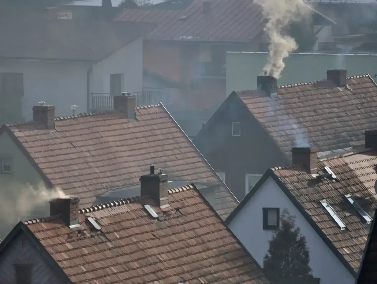 Dym wydobywający się z kominów domów na tle osiedla.